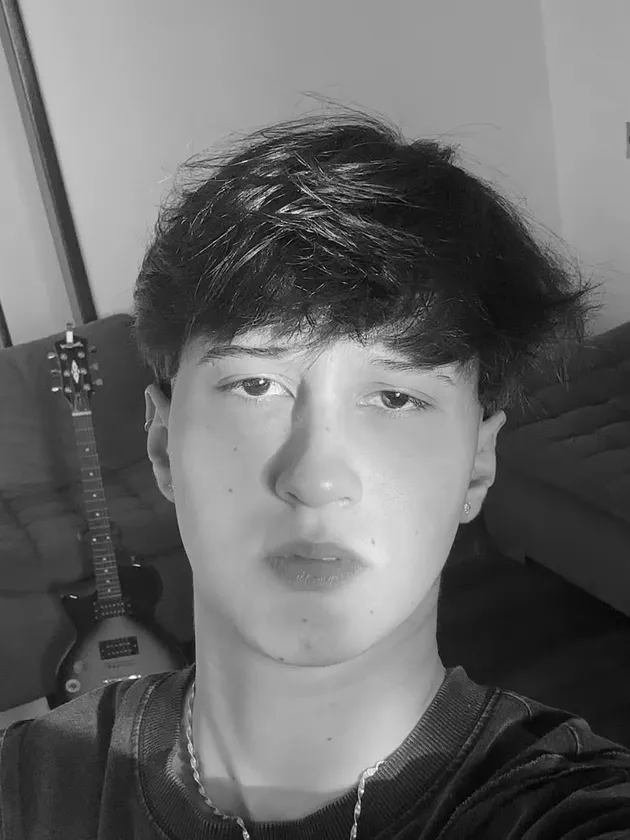 A Aisha numa selfie, em preto e branco. Atrás, uma guitarra encostada no sofá.