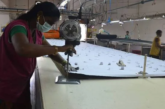 Trabalhadora operando uma máquina de corte sobre camadas de tecido.