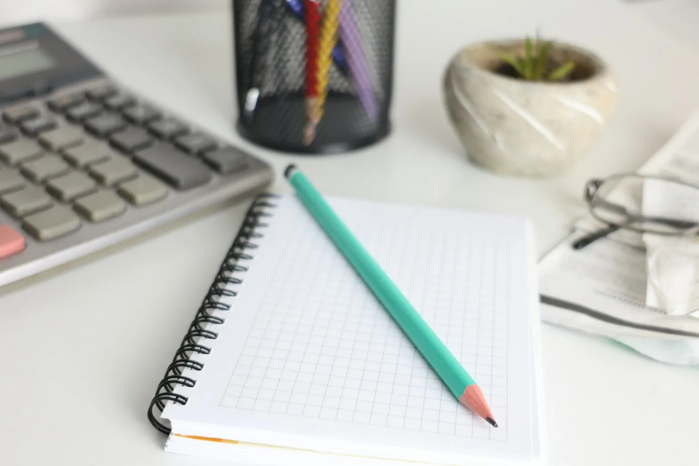 Mesa com calculadora, caderno de anotações e lápis.